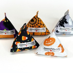 May include: Five Halloween-themed fabric toys in various patterns, including candy corn, pumpkins, and a black cat. Each toy is triangular with a pointed top and features the text "ZiggetyPets.com Happy Pet Happy Home" on a white label.