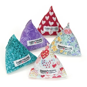 May include: Five triangular catnip toys in various floral and heart patterns. The toys are made of fabric and have a ZiggetyPets.com label with the text "Happy Pet Happy Home".