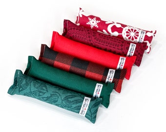 May include: Six catnip toys in various holiday patterns, including red and green plaid, paisley, and snowflakes. Each toy is a long, rectangular pillow with a label that reads "Happy Pets Co."