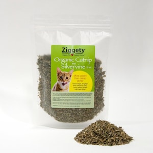 May include: A clear plastic bag filled with dried organic catnip and silvervine, with a green label that reads "Ziggety Organic Catnip and Silvervine". A small pile of the dried herbs sits in front of the bag. The label features a cat.