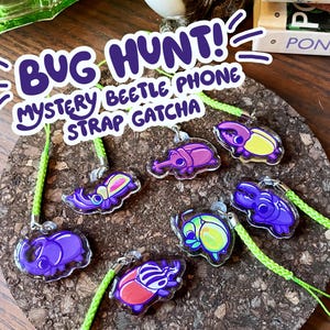 May include: A collection of colourful bug phone charms with green straps. The charms feature different types of beetles, including a purple rhinoceros beetle, a yellow stag beetle, and a pink weevil. The charms are labelled "Bug Hunt! Mystery Beetle Phone Strap Gatcha".