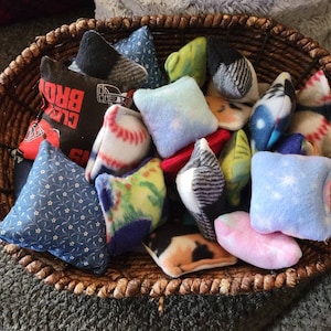 Può includere: Un cesto di vimini pieno di diversi sacchi di fagioli di stoffa dai colori vivaci. I sacchi di fagioli hanno diversi motivi, tra cui palline da baseball, stelle e motivi floreali.
