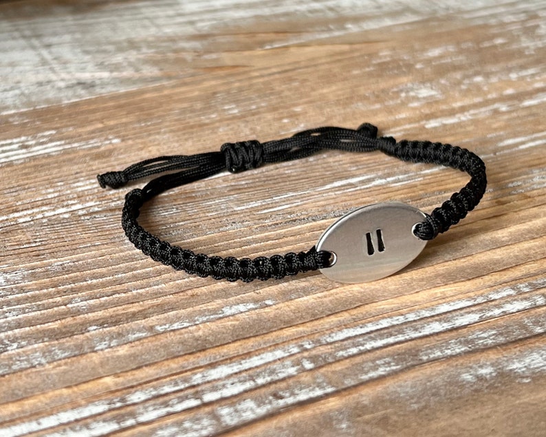 Op de afbeelding: Zwart macram&eacute; armband met een ovale zilveren bedel. De bedel heeft het nummer "11" in een vetgedrukte lettertype. De armband is verstelbaar met een schuifknoopsluiting.