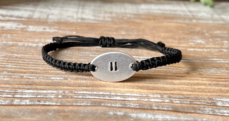 Op de afbeelding: Zwart macram&eacute; armband met een ovale zilverkleurige bedel. De bedel heeft het Romeinse cijfer "II". De armband is verstelbaar met een schuifknoopsluiting.