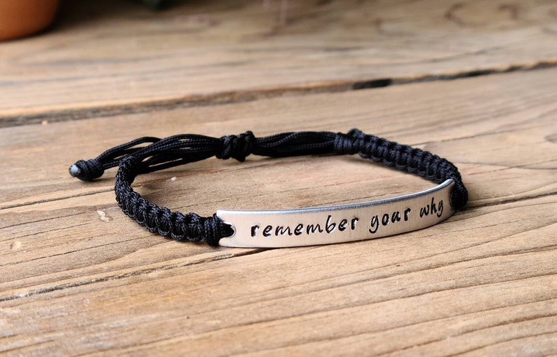 May include: Black braided bracelet with a silver metal tag that reads "remember your why".