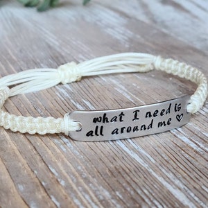 Puede incluir: Pulsera de cuerda blanca con un dije plateado que dice "what I need is all around me" con un s&iacute;mbolo de coraz&oacute;n.