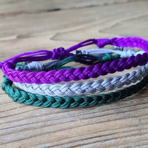May include: A set of three braided friendship bracelets in green, gray, and purple.