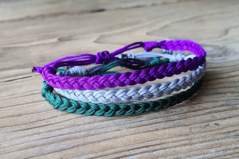 May include: A set of three braided friendship bracelets in green, gray, and purple.