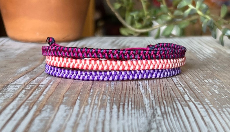 May include: Three braided bracelets in purple, red and white, and black and pink.