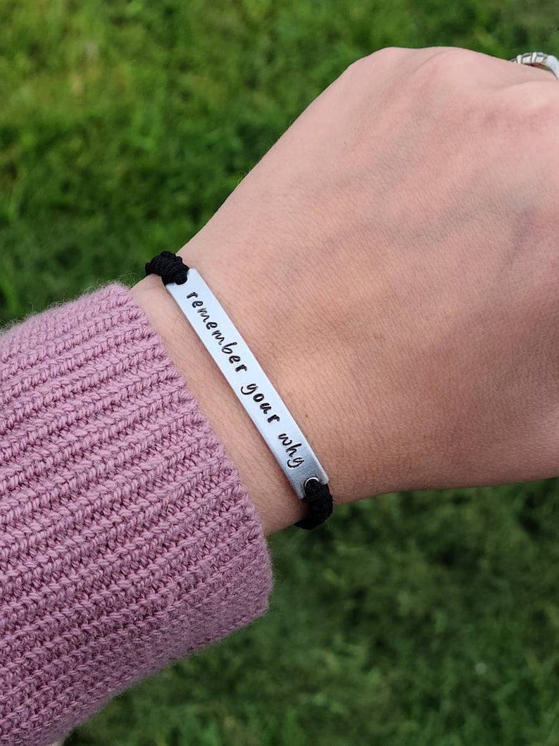 May include: A black elastic bracelet with a silver metal bar that reads "remember your why".
