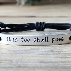 May include: Black braided cord bracelet with a silver charm that reads "this too shall pass".