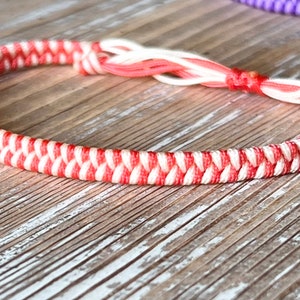 May include: A red and white braided friendship bracelet with a knot at the end.