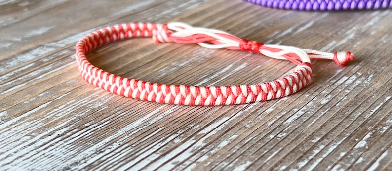 May include: A red and white braided friendship bracelet with a knot at the end.