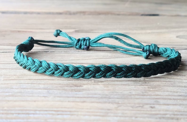 May include: A dark green braided cord bracelet with adjustable closure. The bracelet is made of a soft, durable cord and is perfect for everyday wear.
