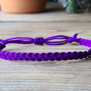 May include: A purple braided friendship bracelet with adjustable knots at the ends.