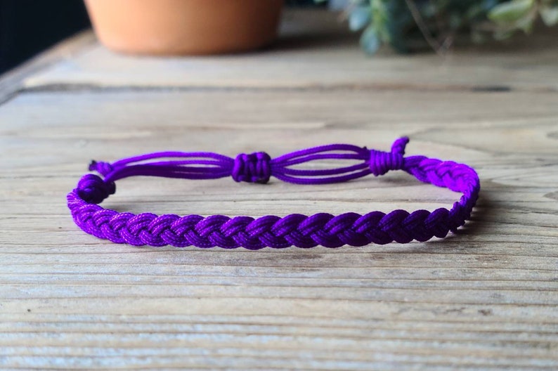 May include: A purple braided friendship bracelet with adjustable knots at the ends.