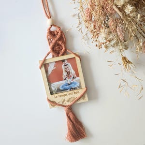 Può includere: Una cornice per foto in legno con un fiocco di macramè appeso in alto. La cornice contiene una foto di una donna e un bambino. La cornice ha il testo "Le temps est bon" e un codice Spotify stampato su di essa.