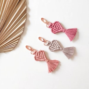 Peut inclure: Trois porte-clés en forme de cœur avec des glands. Les porte-clés sont en macramé et sont disponibles en rose et beige.