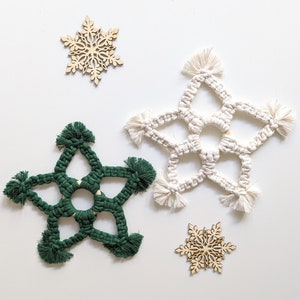 Puede incluir: Tres adornos de estrella de macramé hechos a mano en diferentes colores. Una estrella blanca, una estrella verde y una estrella de madera.
