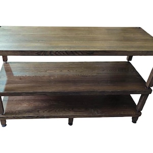 May include: A three-tiered wooden shelf unit with a dark brown finish. The shelves are made of solid wood and have a natural grain pattern. The unit has a simple, modern design and is perfect for displaying books, plants, or other decorative items.