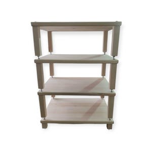 May include: A light-colored, three-tiered wooden shelf unit. The shelves are rectangular and supported by square legs. The unit is designed for storage or display, with a simple, minimalist aesthetic.