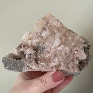 May include: A cluster of white and pink crystals with a rough, gray base. The crystals are clustered together in a natural formation.