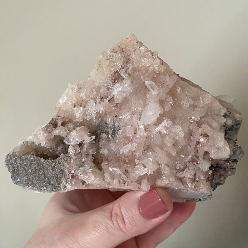 May include: A cluster of white and pink crystals with a rough, gray base. The crystals are clustered together in a natural formation.