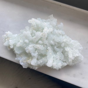 May include: A cluster of white and light green crystals with a rough, textured surface.