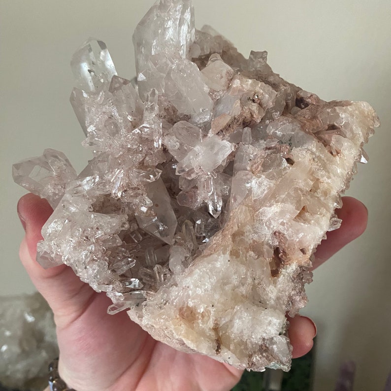 May include: A large cluster of clear quartz crystals with a natural, rough, and textured surface. The crystals are clustered together in a dense formation, creating a unique and eye-catching display.