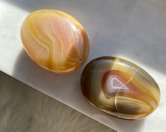 May include: Two agate palm stones, one with brown and white banding and the other with yellow and white banding.