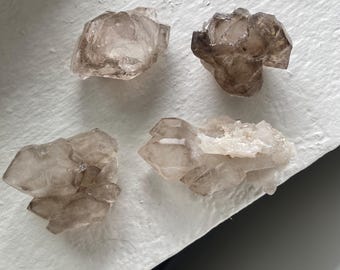 May include: Four smoky quartz crystal clusters with various shapes and sizes. The crystals are translucent and have a light brown color.