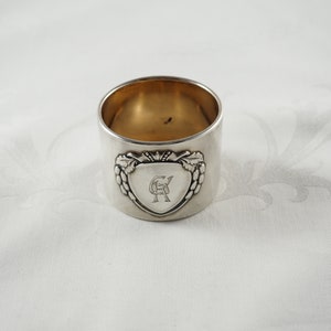 Può includere: Anelli tovagliolo in argento con un design a forma di cuore e le iniziali "GR" incise all'interno. L'anello ha un motivo decorativo a vite attorno al cuore.