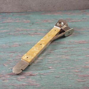 May include: A vintage multi-tool knife with a cream-coloured, patterned handle and silver-toned metal components. The knife features a bottle opener, a small hammer, and a blade. The handle is secured with small, dark rivets.