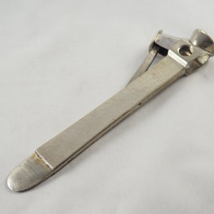 May include: A silver metal pipe tamper with a built-in cutter. The tamper has a long, flat handle and a rounded head with a hole in the centre.