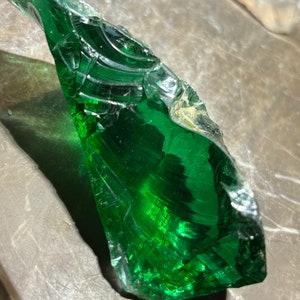 Puede incluir: Un gran fragmento de vidrio verde con una superficie lisa y pulida. El fragmento tiene un patrón único en espiral y es translúcido.