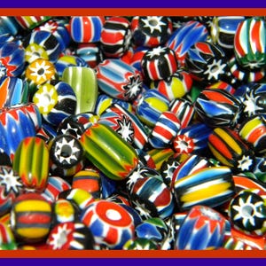 May include: A collection of colorful glass beads with various patterns, including stripes, swirls, and stars. The beads are a mix of red, blue, green, yellow, black, and white.