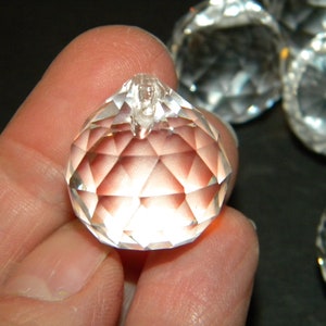 May include: A close-up of a clear crystal ball with a faceted surface. The ball is being held in a hand.