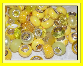 May include: A collection of assorted yellow and lime green beads, each featuring a central silver-toned metal core. The beads exhibit various textures, including smooth, translucent, opaque, glittery, and bumpy finishes, all clustered together.