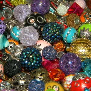 May include: A large assortment of colorful and patterned beads, including glass, metal, and plastic beads. The beads are in various shapes and sizes, and some have intricate designs.