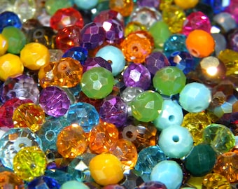 May include: A collection of multi-colored faceted glass beads in various hues including yellow, orange, red, purple, blue, and green. Each bead features a central hole and a reflective, multi-faceted surface that catches light.