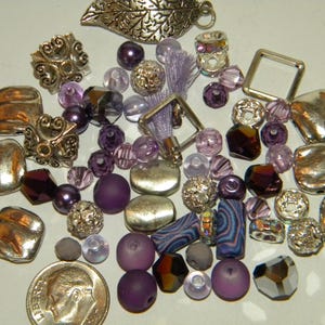 May include: Assortment of purple and silver beads and charms, including metal squares, leaves, and flower shapes.