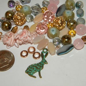 May include: A collection of colorful glass and metal beads, including pink, green, gold, and brown beads. There is also a small metal rabbit charm.