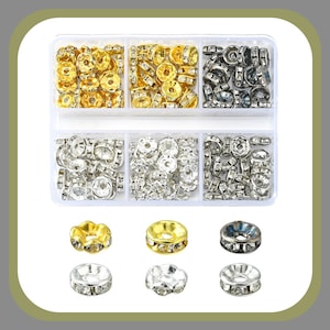 May include: A clear plastic storage box with six compartments filled with gold, silver, and black metal bead caps. Each cap is adorned with clear rhinestones. The box is on a white background.