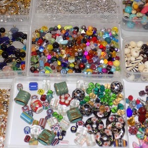 May include: A collection of beads in various shapes, sizes, and colors, displayed in clear plastic containers. The beads include round, faceted, and patterned designs, with a mix of materials like glass and metal. The assortment offers a wide range of options for jewelry making and crafting.