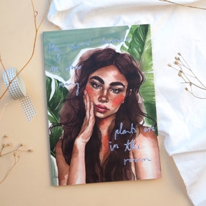 May include: A journal featuring a watercolour illustration of a woman with long brown hair and red cheeks. The cover has the text "My mood depends on how many plants are in the room" in blue script.