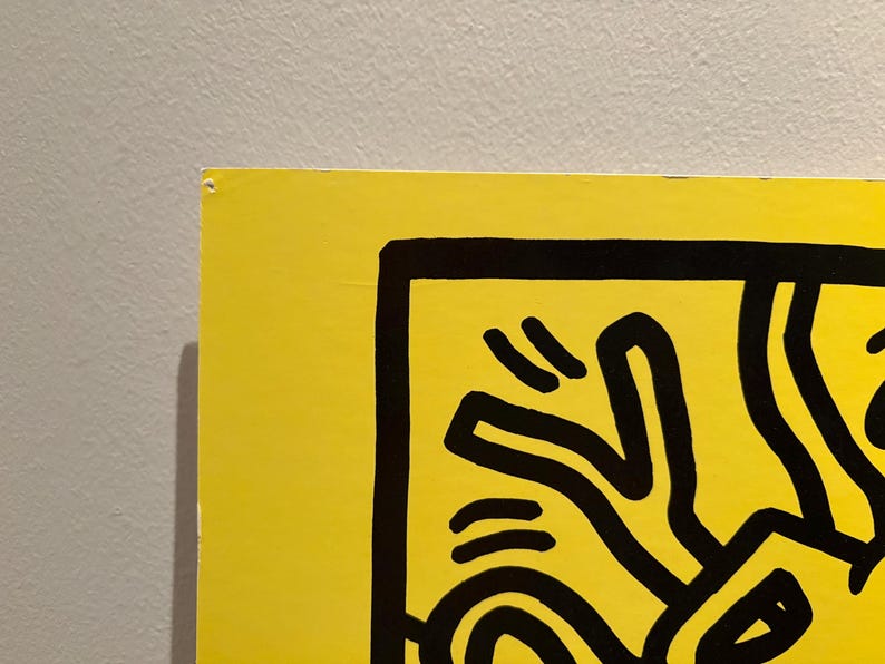 Puede incluir: Una secci&oacute;n de una obra de arte amarillo vibrante con l&iacute;neas negras audaces. La obra presenta una figura humana estilizada, parte de un dise&ntilde;o m&aacute;s amplio. La pieza est&aacute; montada en una pared gris neutra, creando un contraste llamativo.