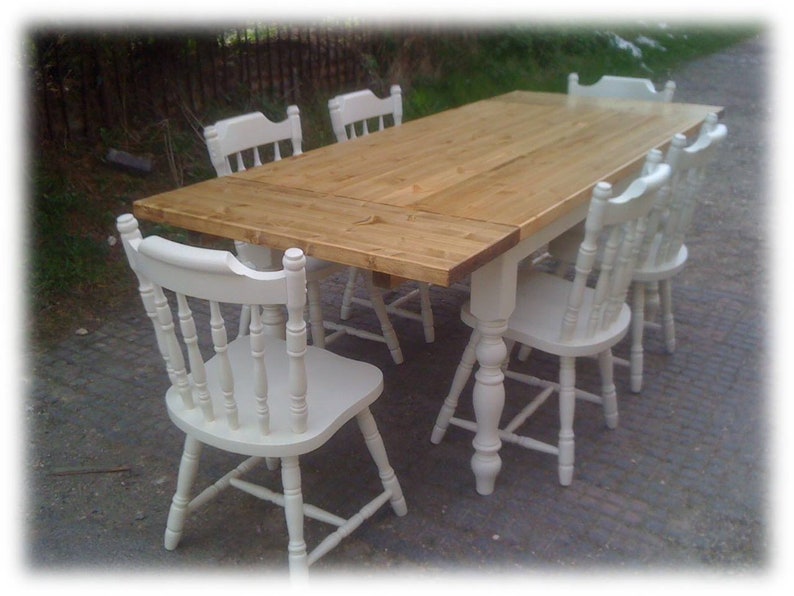 May include: A wooden table with a natural finish and six white chairs. The table has a rectangular top and a single pedestal base. The chairs have a simple design with a slatted back and turned legs.
