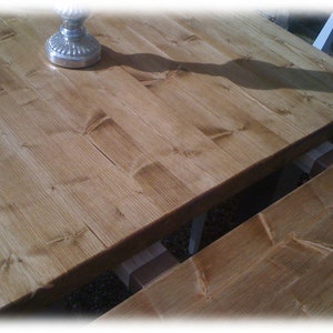 May include: A close-up of a wooden table top with a natural wood finish. The table top is made of planks of wood that have been joined together. The wood has a warm, honey-colored hue.