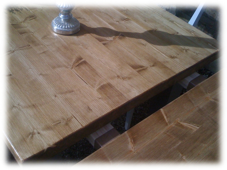 May include: A close-up of a wooden table top with a natural wood finish. The table top is made of planks of wood that have been joined together. The wood has a warm, honey-colored hue.
