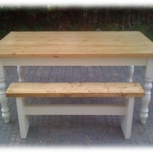 May include: A white farmhouse style table with a natural wood top and a matching bench. The table has turned legs and the bench has a simple design.